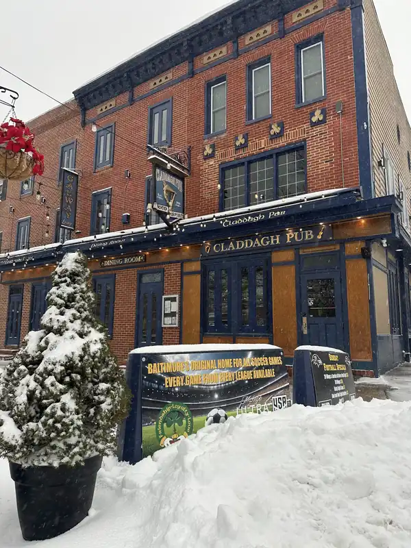 The Claddagh Pub corner sign on a snowy morning, with a sandwich board out for the soccer on the sidewalk