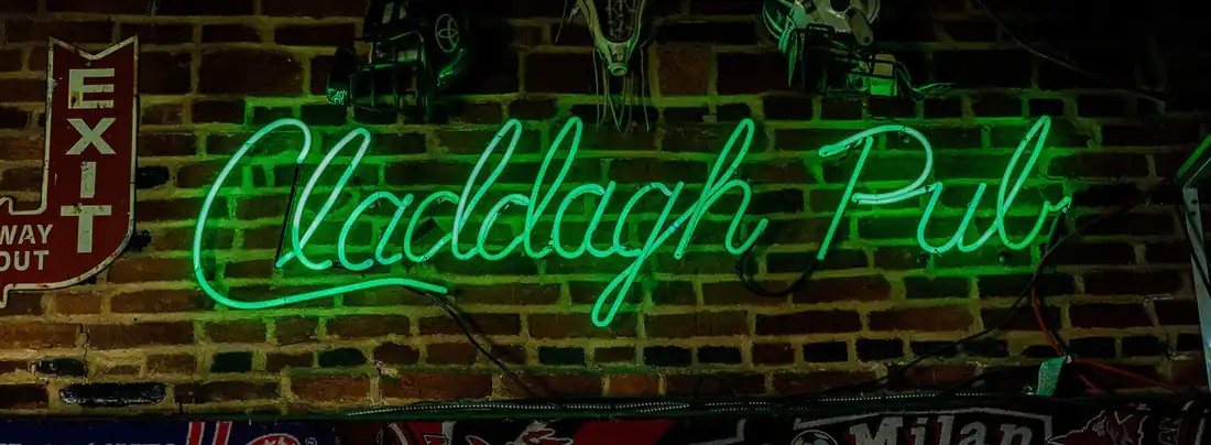 Green neon script reading Claddagh Pub on the brick wall inside